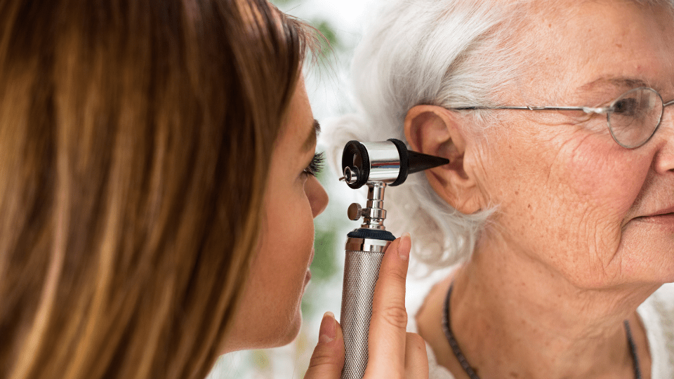 Hearing specialist examining an elderly woman’s ear with an otoscope