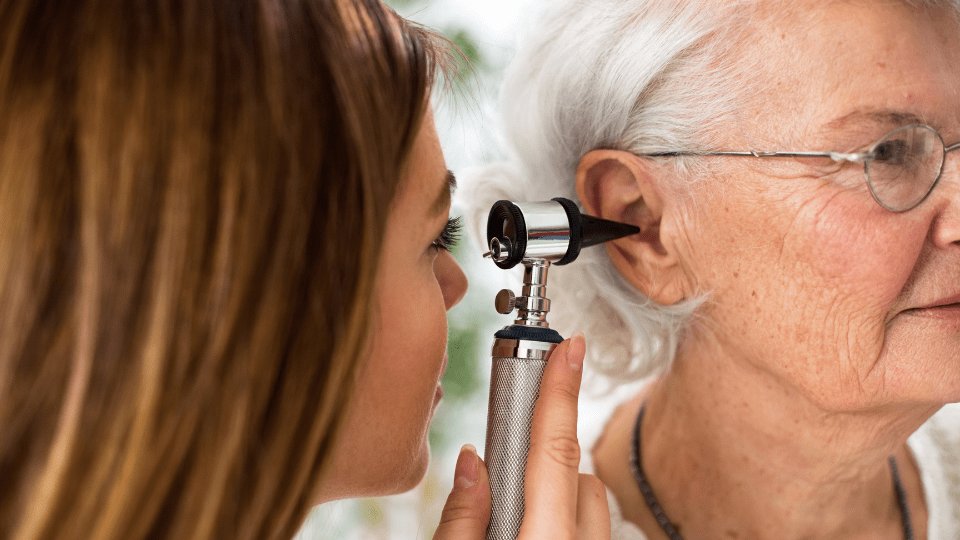 Hearing specialist examining an elderly woman’s ear with an otoscope