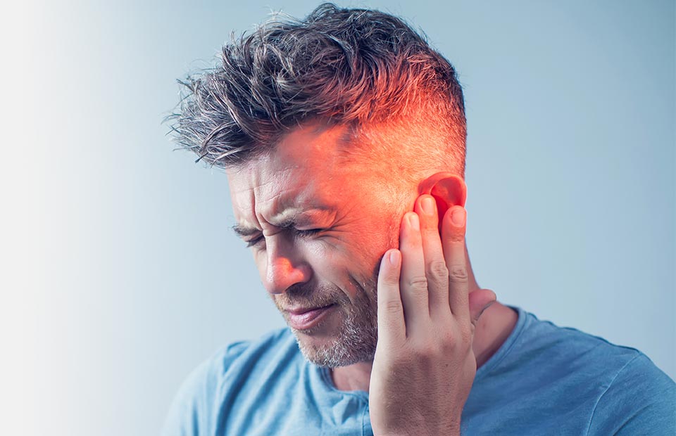 A person touches their ear with visible red irritation or discomfort, suggesting hearing issues. The blue gradient background emphasizes the focus on hearing health, relevant for Audika’s hearing care services.