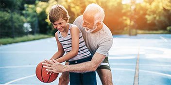 Grandfather teaching grandson to play basketball outdoors