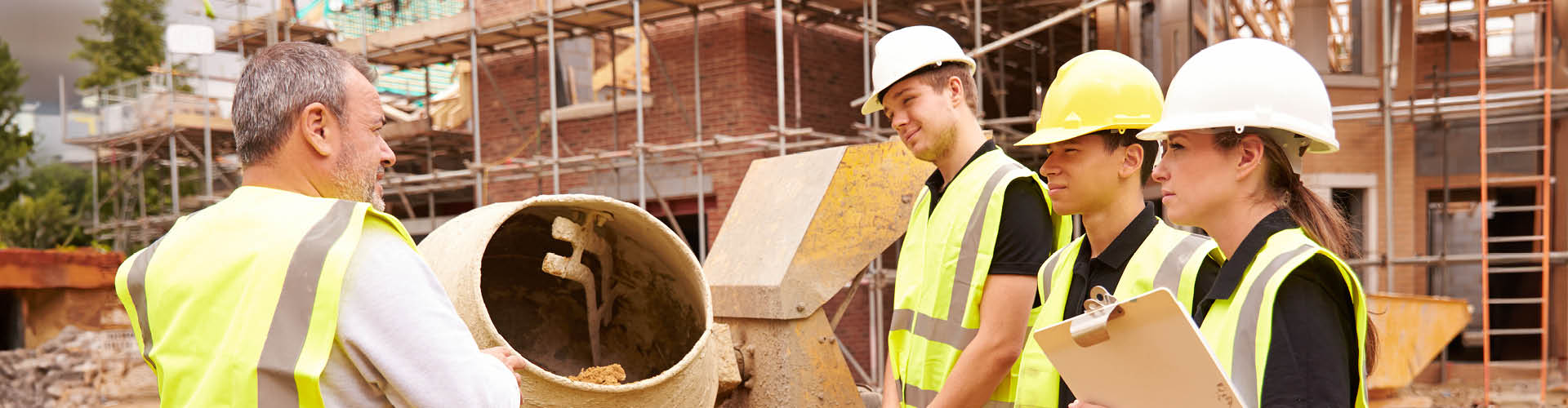 construction workers wearing safety gear on a building site discussing work near a cement mixer