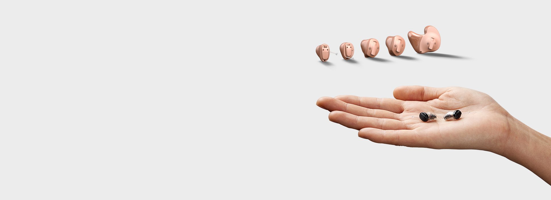 Hand holding two IIC Oticon Own hearing aids in palm