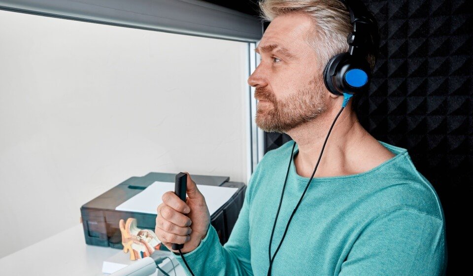 Man undergoing hearing test in soundproof booth while wearing headphones and holding response button