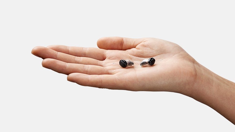 Hand holding Oticon Own IIC hearing aids, showcasing their small and discreet design