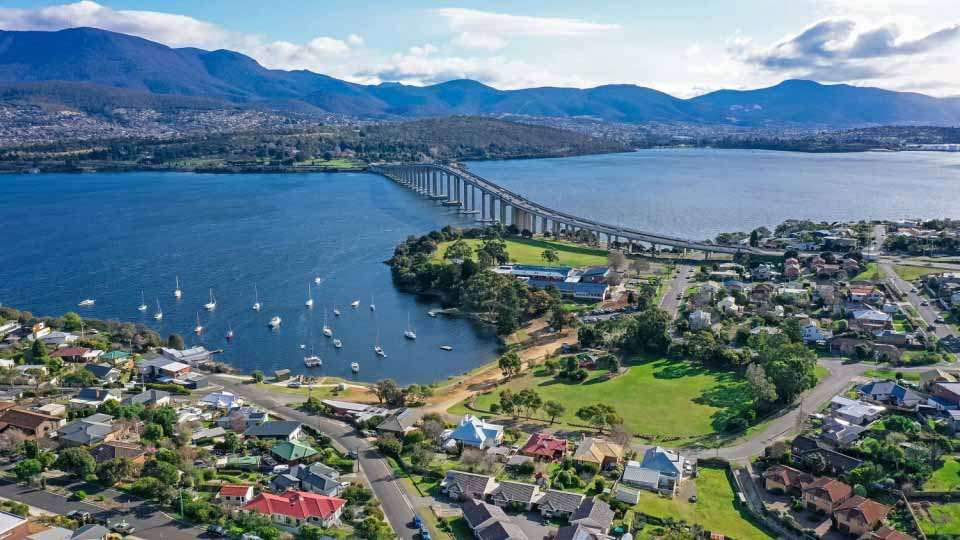Hobart waterfront view with the Tasman Bridge, residential areas, and surrounding mountains.