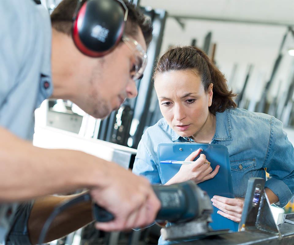 worker using loud machinery while colleague holds a clipboard in an industrial setting