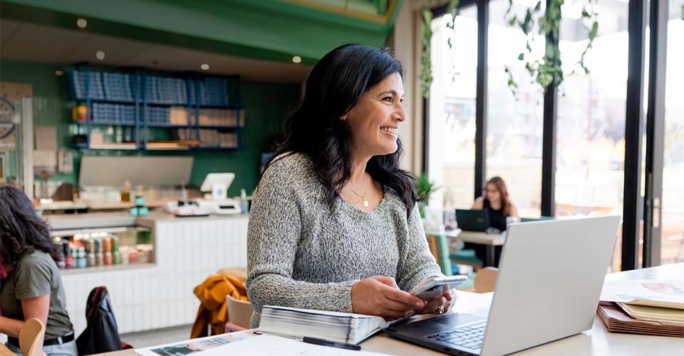 Woman multitasking with phone and laptop at a cozy café table