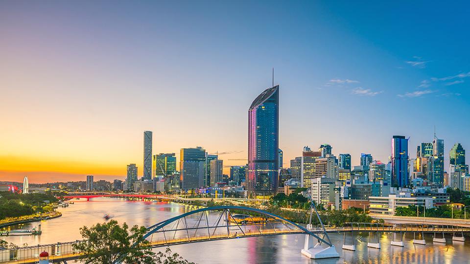 Skyline of Brisbane at sunset with the Brisbane River and modern bridges in the foreground.