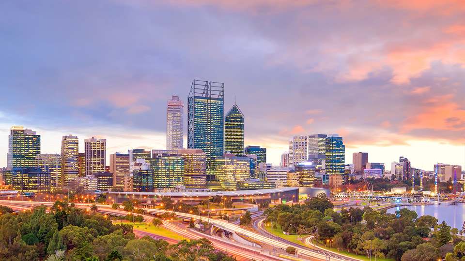 Skyline of Perth, Australia at sunset with city buildings illuminated and vibrant skies in the background.