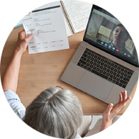 Senior professional participating in a video call while reviewing a document at a desk.