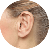 Receiver-in-the-ear (RITE) hearing aid worn behind the ear of a woman with tied-back hair