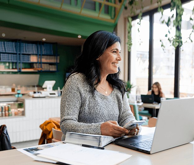 woman-using-smartphone-while-working-on-laptop-in-modern-cafe