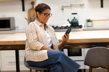 Woman_sitting_in_her_kitchen_using_her_mobile_phone