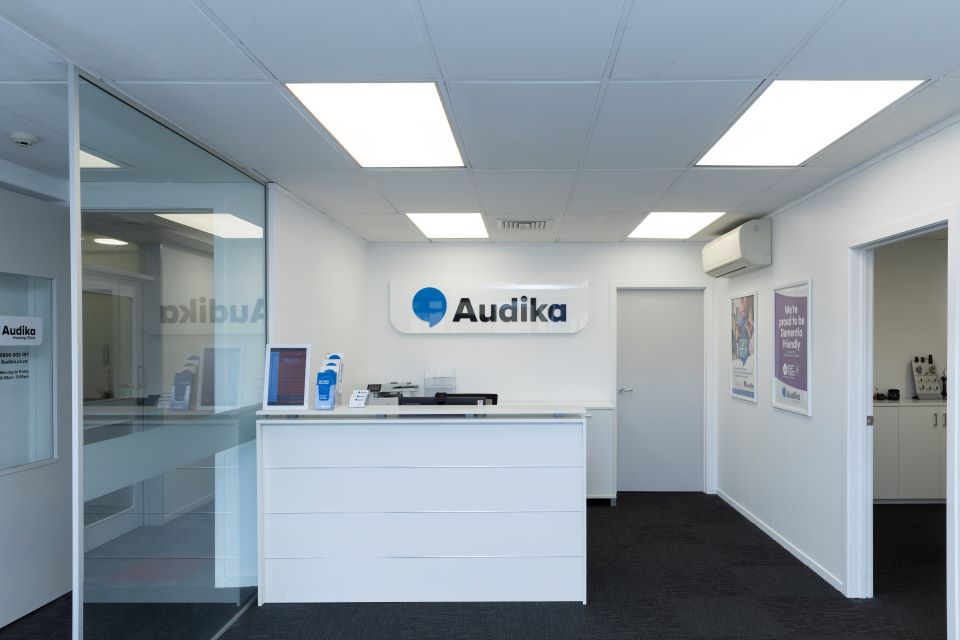 Reception area of Audika's Hamilton clinic with a modern white desk, branded signage, and informational posters on the walls.