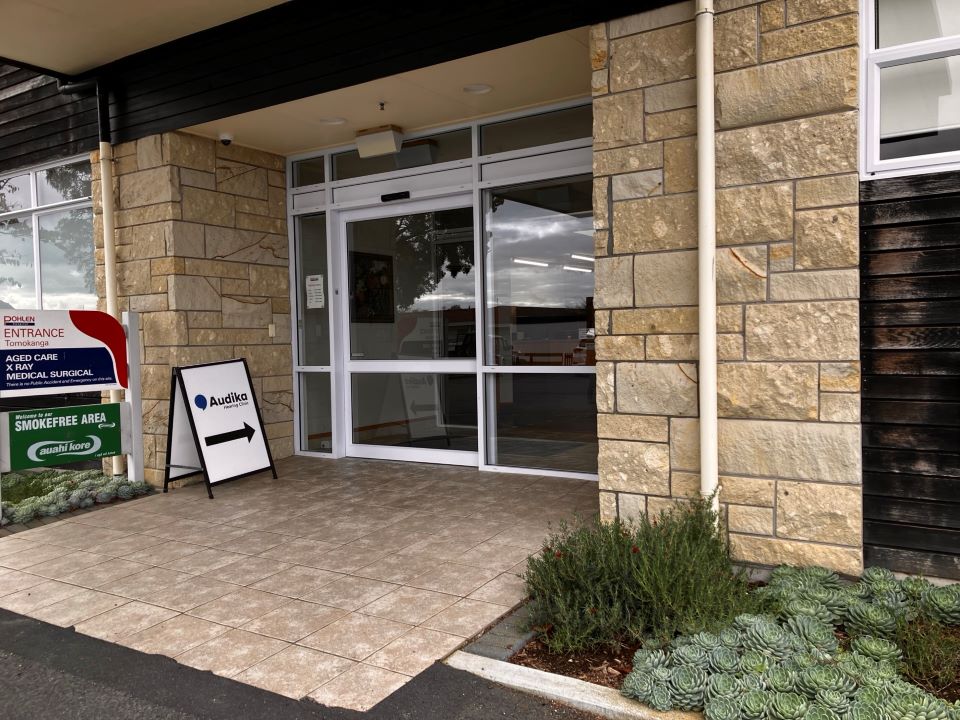 Entrance of Audika Hearing Aid Clinic in Matamata showing a directional sign and surrounding exterior features.