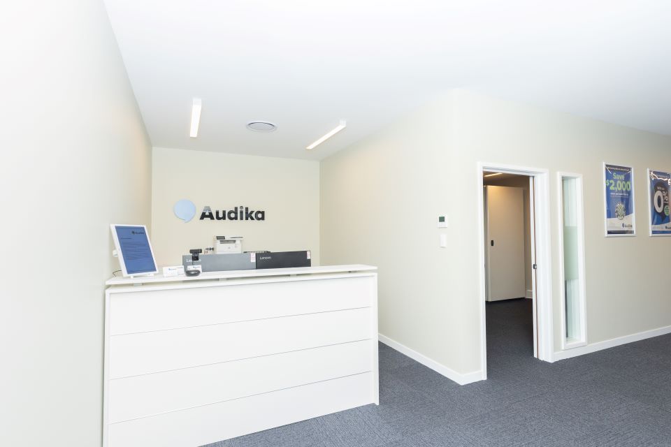 Reception area of Audika Hearing Clinic in Papanui, featuring a clean and modern white desk with promotional posters on the walls.