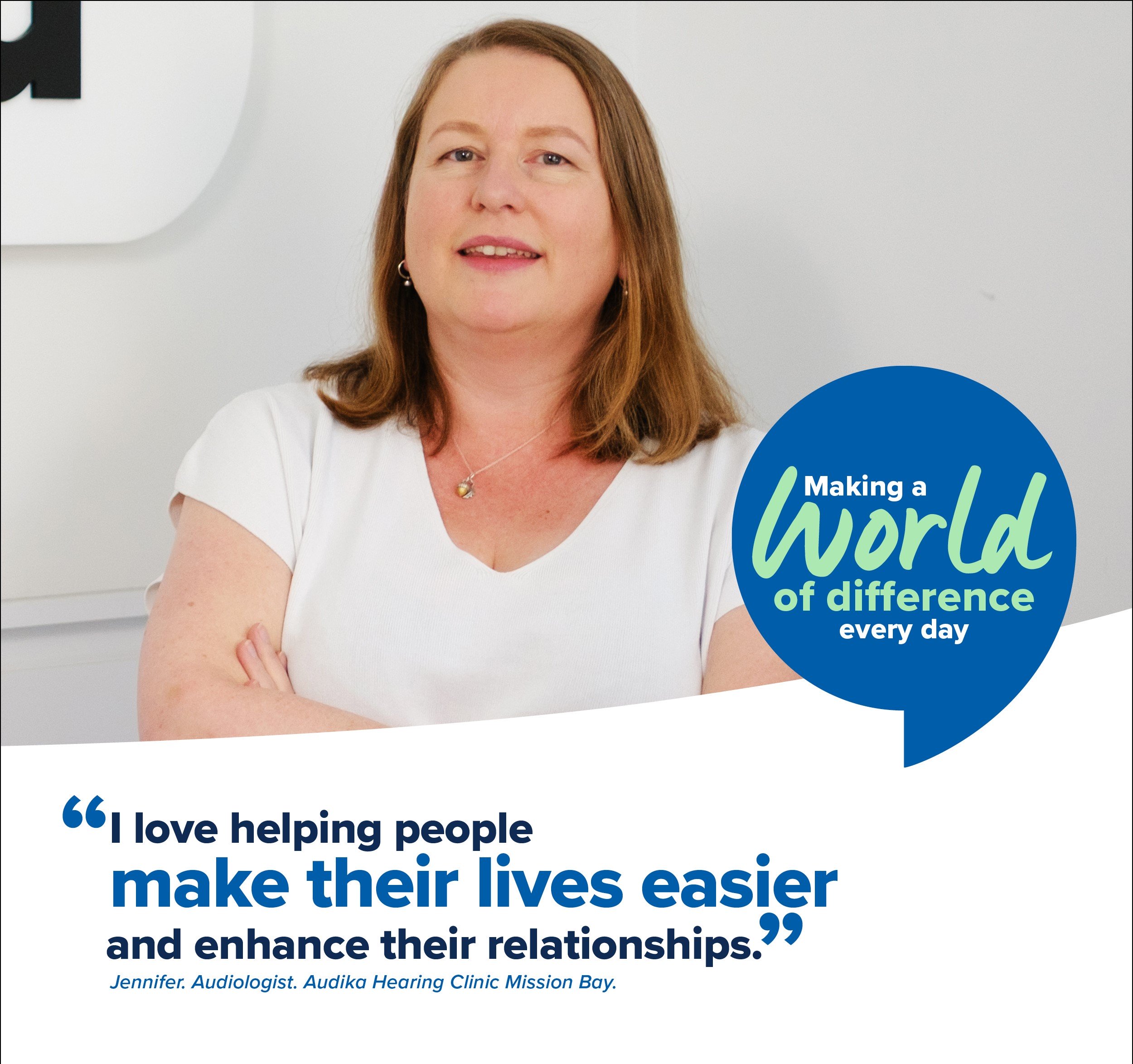 Jennifer, audiologist at Audika Hearing Clinic Mission Bay, standing in front of clinic branding with quote about helping people improve their lives and relationships.