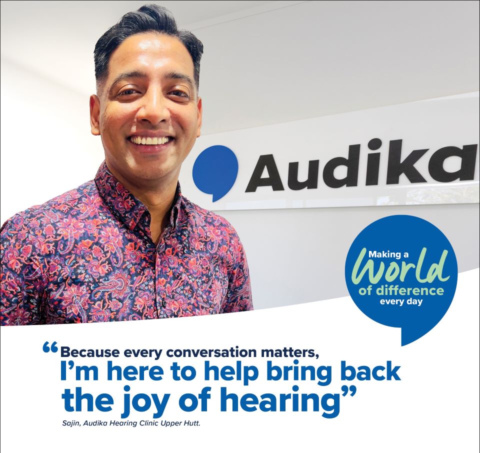 Sajin, hearing care clinician at Audika Upper Hutt, standing in front of the clinic sign with the tagline ’Because every conversation matters, I’m here to help bring back the joy of hearing.’