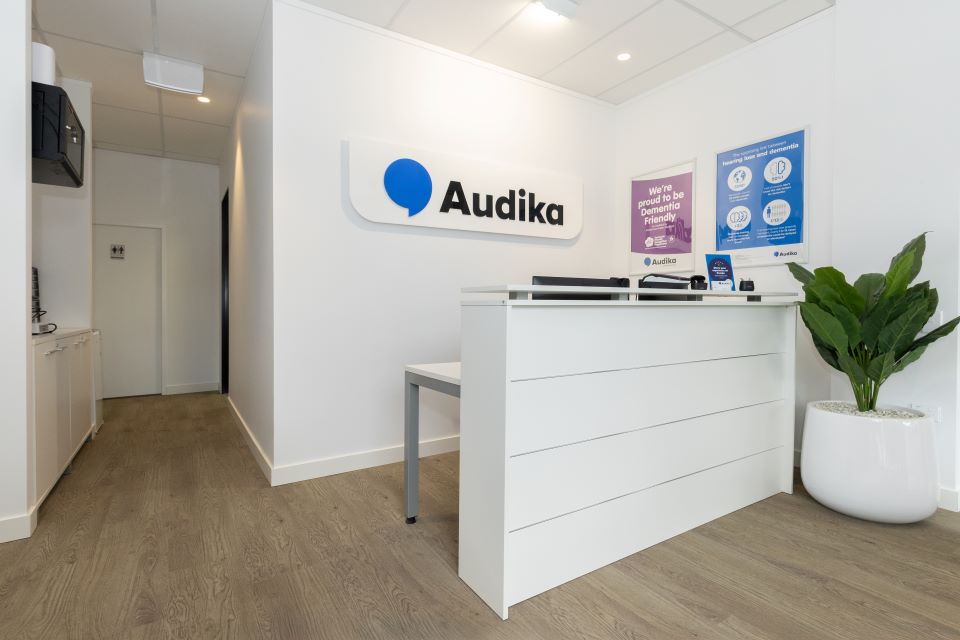Audika hearing clinic reception area in Rangiora with sleek white desk, branded signage, educational posters, and indoor plant.