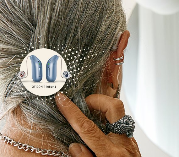 Woman with grey hair adjusting her hearing aid, showcasing Oticon Intent hearing aids with sleek design and advanced technology.