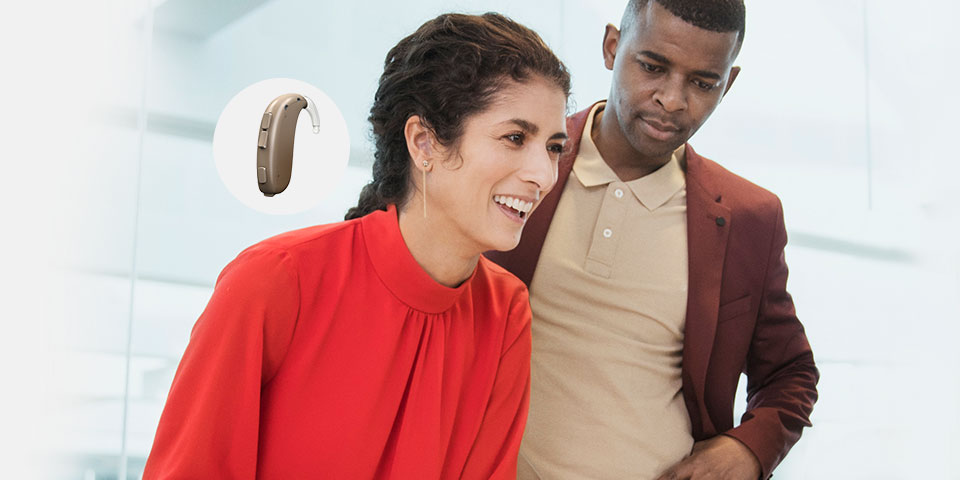 Xceed hearing aid displayed alongside two people smiling in a modern setting.