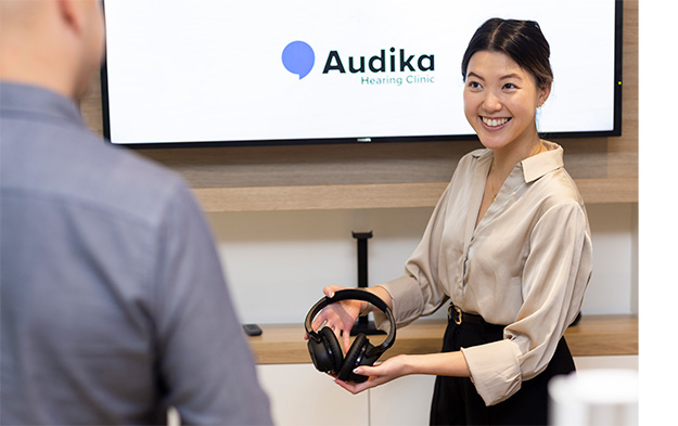 Audika hearing care professional providing headphones to client for hearing assessment