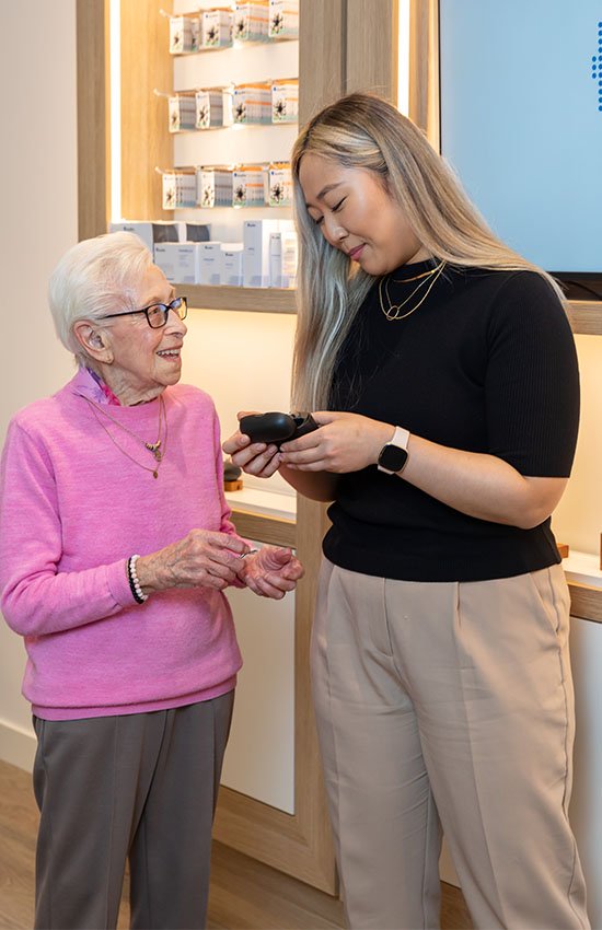 audiologist assisting older woman with hearing aids in a hearing care clinic