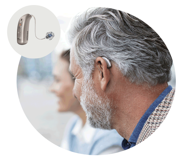 A silver Oticon hearing aid is discreetly worn behind the ear of a white-haired man engaging in conversation. Inset: close-up of the Oticon hearing aid with a miniFit receiver.