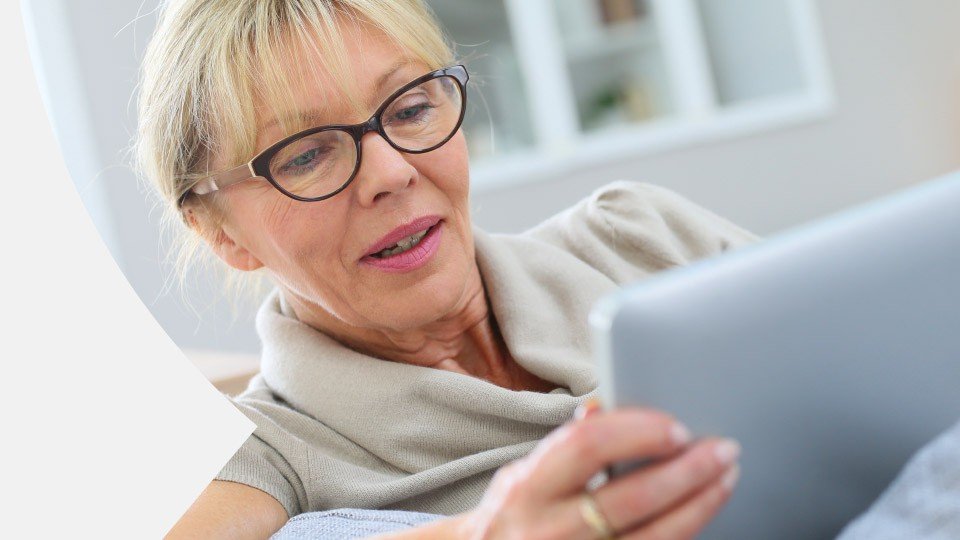 Woman smiling while using a tablet indoors.