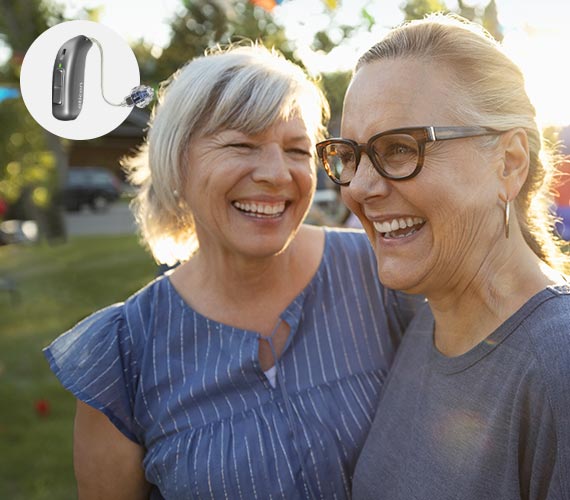 Smiling couple outdoors with a hearing aid device displayed.