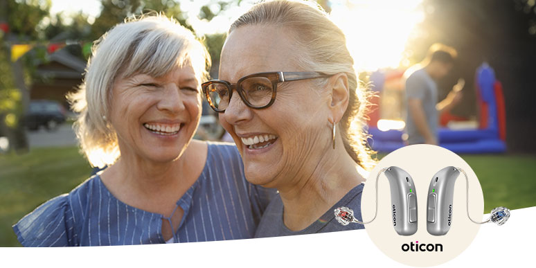 Two older adults with blurred faces stand outdoors in a sunlit park, smiling and embracing. Featured nearby is a circular inset showcasing Oticon hearing aids, promoting advanced hearing solutions.