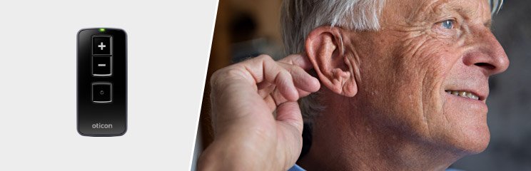 Man adjusting hearing aid with Oticon remote control nearby.
