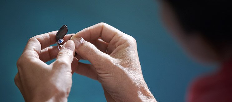 Hands replacing a battery in a hearing aid