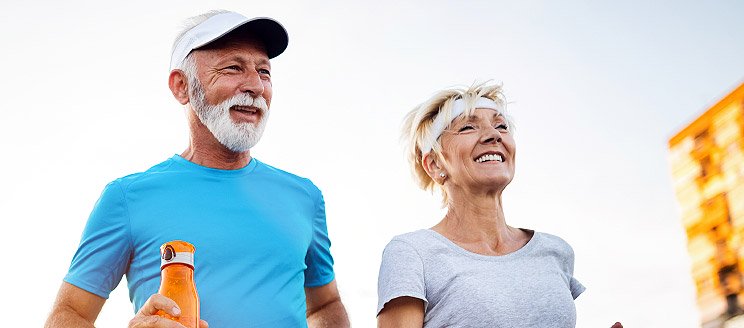 Elderly couple jogging outdoors on a sunny day, promoting active and healthy lifestyles.