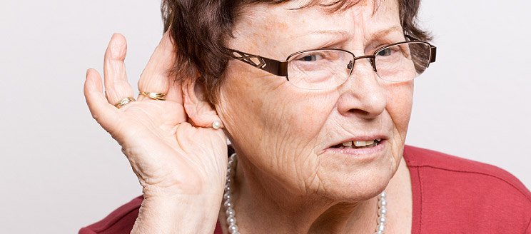 Elderly woman cupping hand to ear as if struggling to hear clearly.