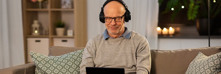 Man wearing headphones while using a laptop on a sofa in a cozy living room setting.