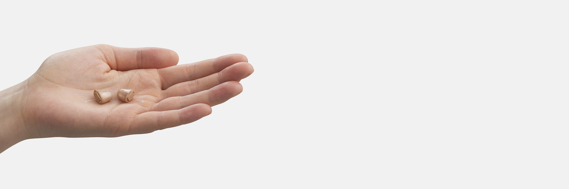 A hand holds two small, discreet in-the-ear hearing aids against a plain white background, emphasizing advanced hearing care technology. No text or identifiable brands are visible.