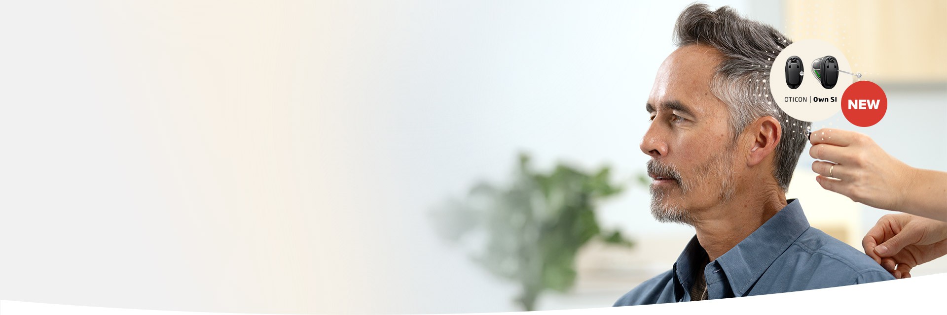 A person is fitted with a hearing aid by a professional in a hearing clinic. The image highlights ’Oticon Own S1 NEW’ hearing aids with a clean, light background featuring indoor plants.