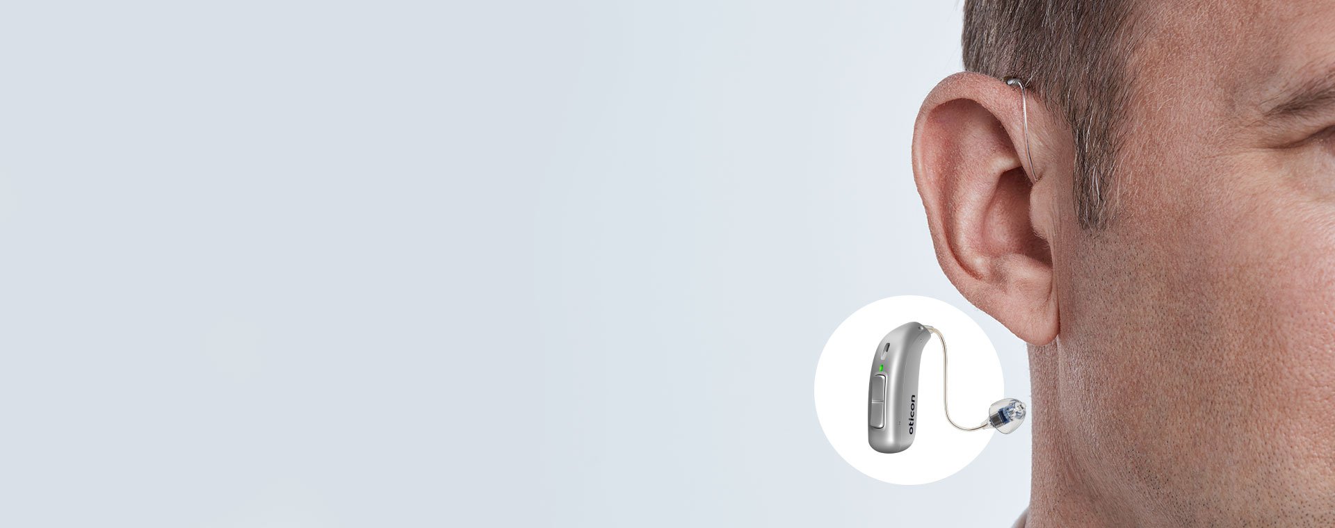 Hearing aid positioned behind the ear of a man, with a close-up of the device showcasing its design and features.