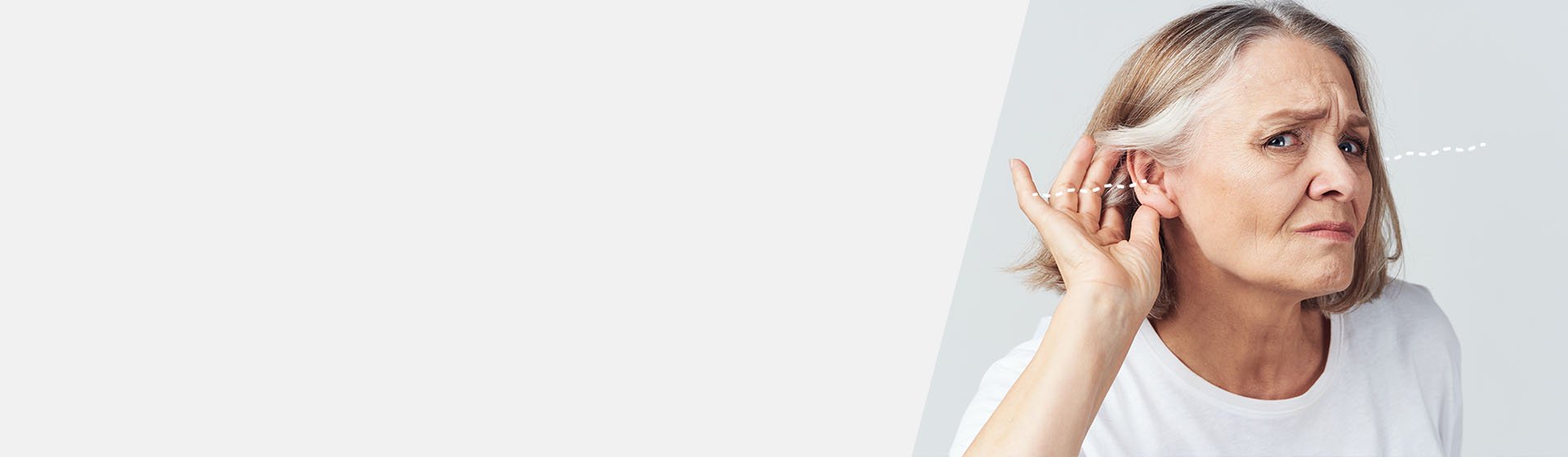 Woman with gray hair holding her hand to her ear, demonstrating hearing difficulty.