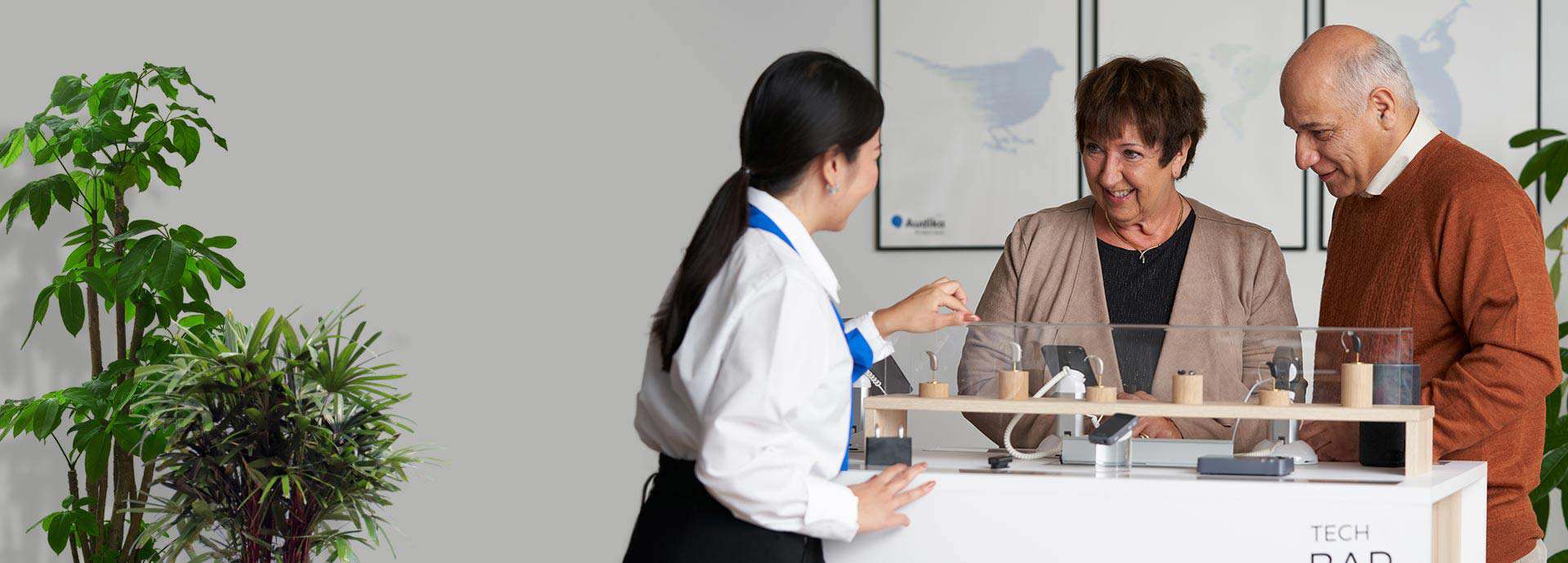 Clinician assisting a couple with hearing aid options displayed on a counter.