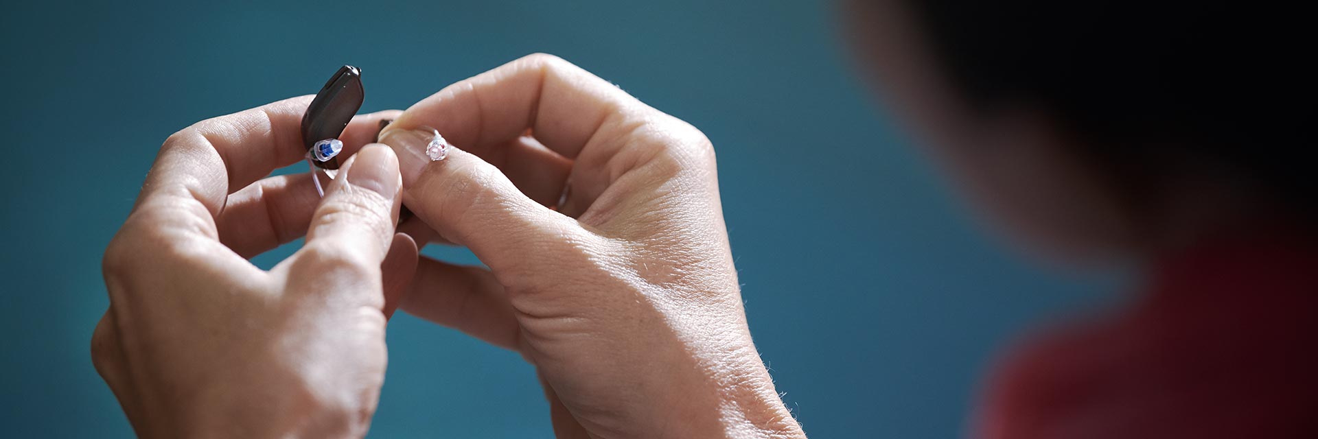 Hands replacing hearing aid batteries against a blue background.