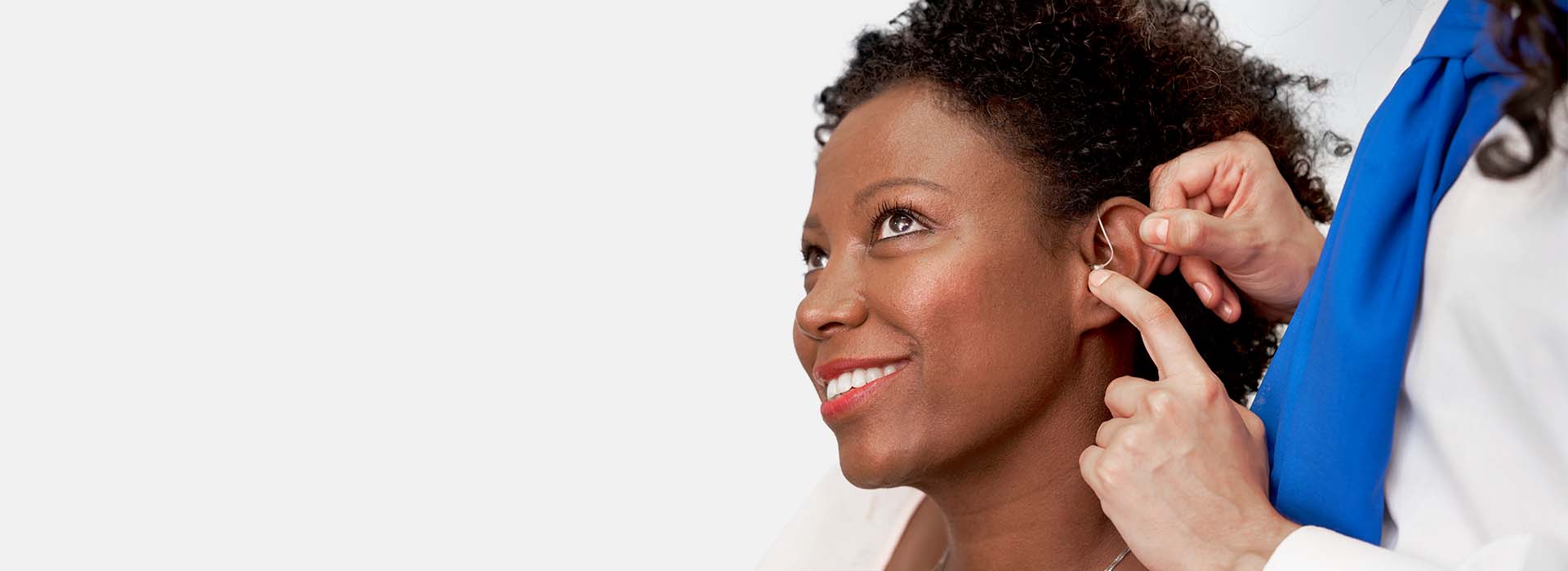 Audiologist fitting hearing aid into woman’s ear