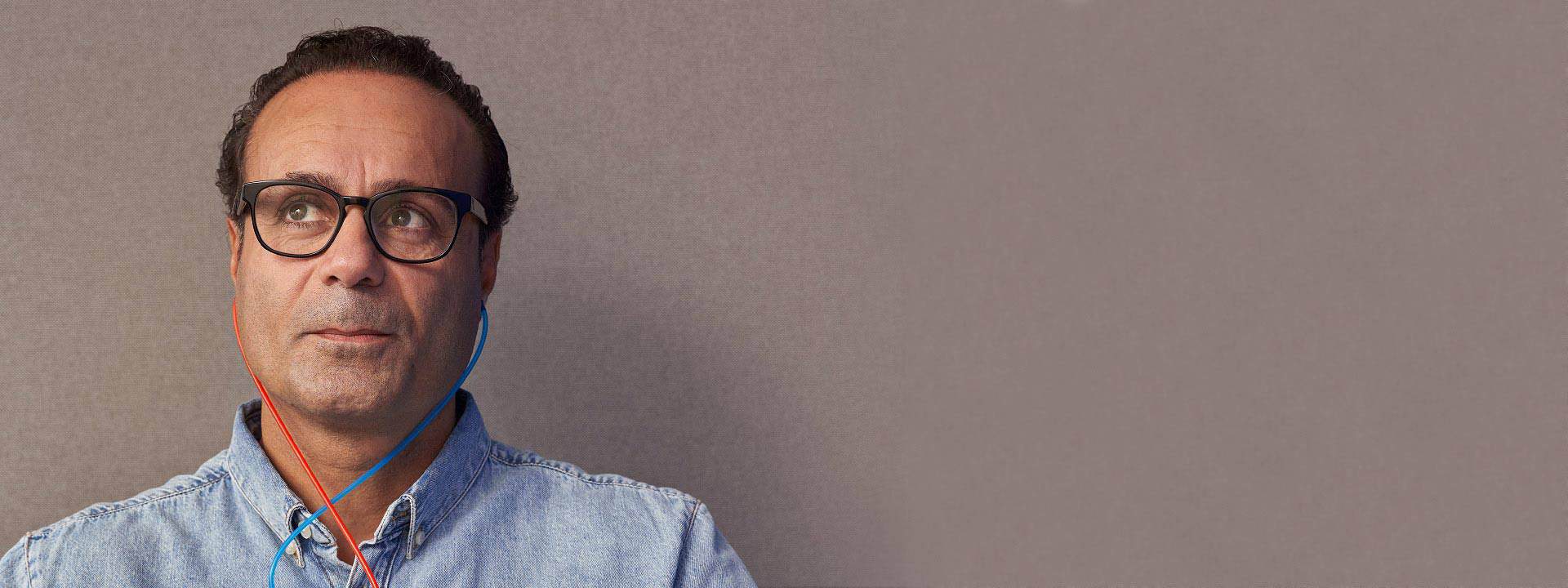 Man wearing earphones with wires crossing over a denim shirt.