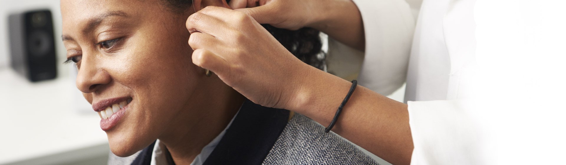 Audiologist fitting a hearing aid onto a woman.