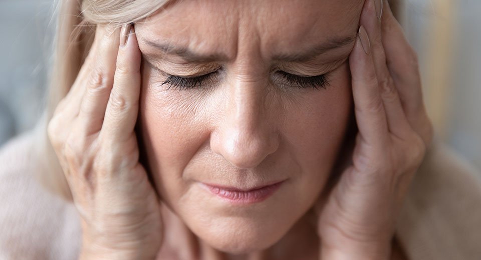 Woman holding her head with both hands, experiencing discomfort from untreated hearing loss.