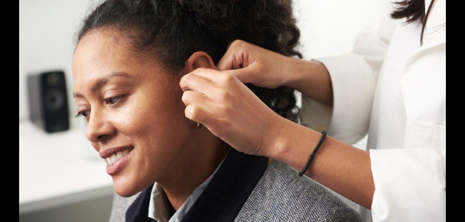 Woman being fitted with a hearing aid by a hearing care specialist.