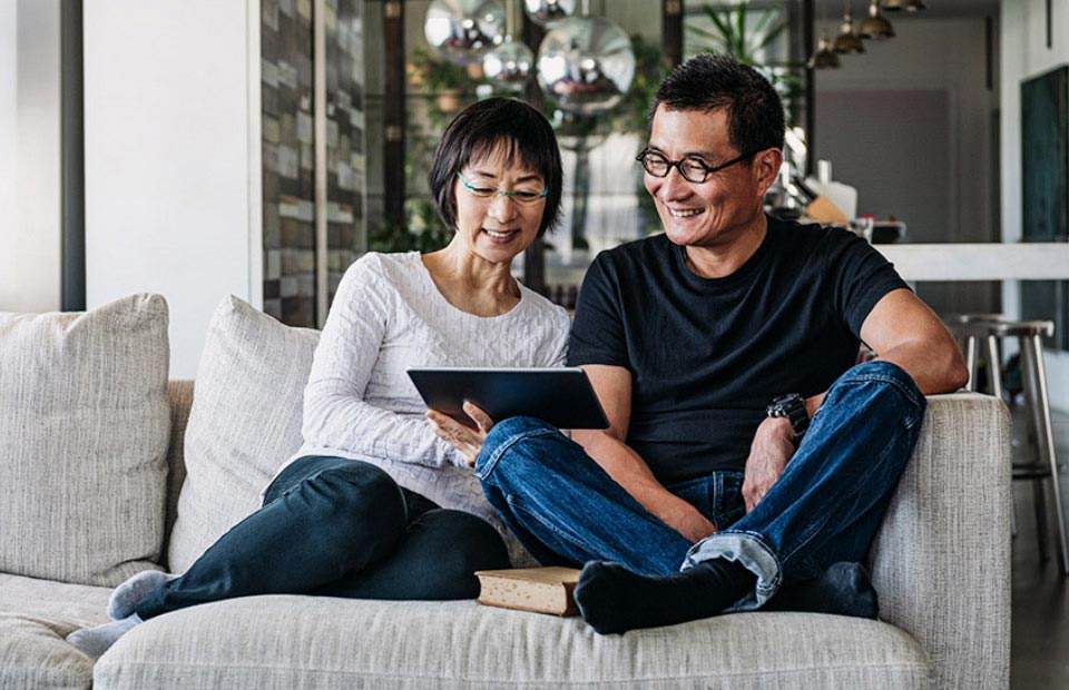 Couple sitting on a sofa at home, sharing a tablet.