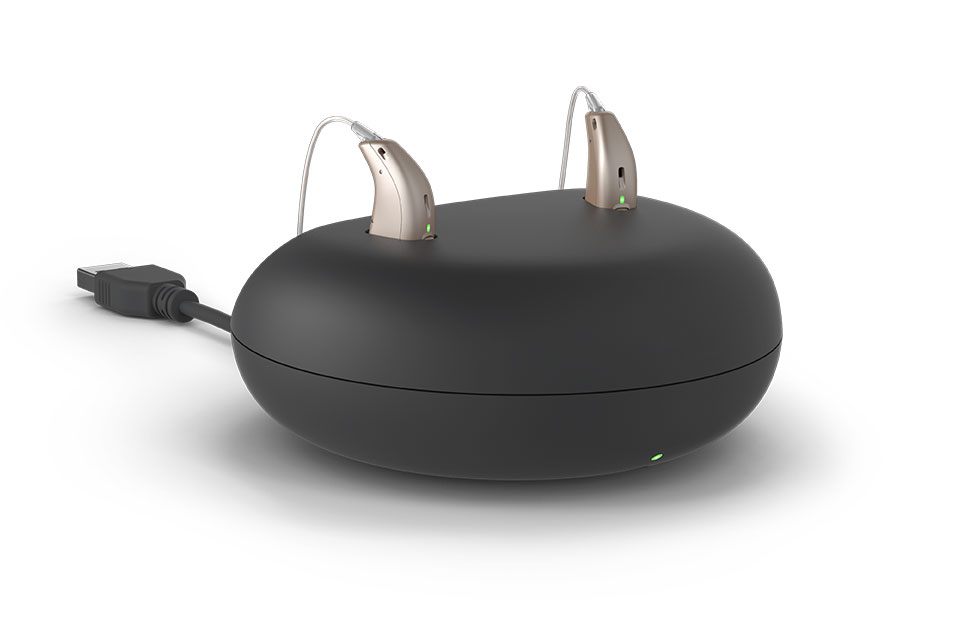 Rechargeable hearing aids placed in a black charging case with a connected USB cord.