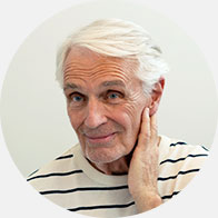 Senior woman with short white hair touching her ear, possibly indicating difficulty hearing or ear discomfort.